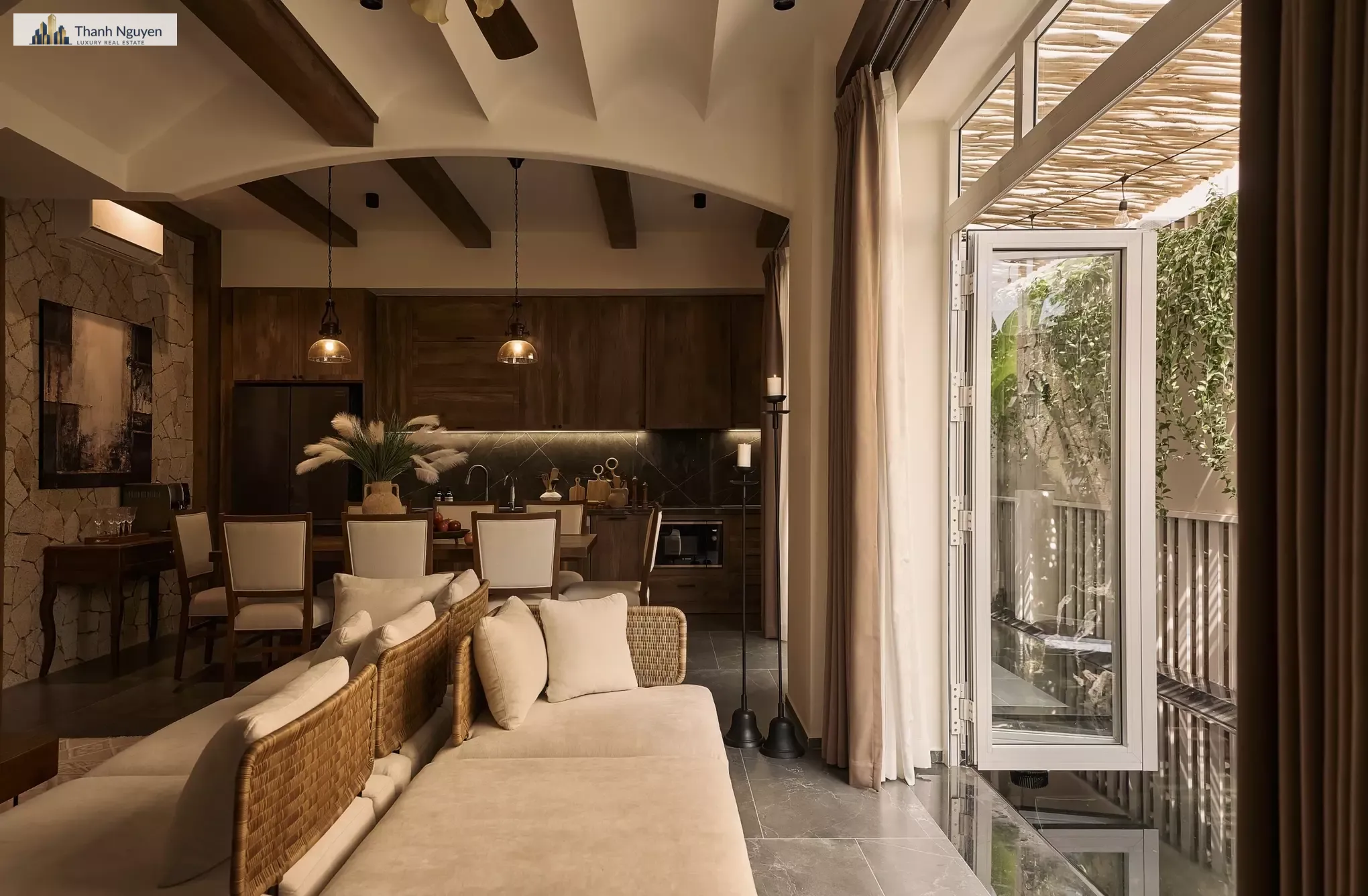 Thiết Kế Nhà Phố Phong Cách Đồng Quê Âu Mỹ: Hài Hòa Khí Hậu Nhiệt Đới Việt Nam 2 Căn biệt thự 183 m2 tại TP HCM được tổ chức liên thông giữa phòng khách, bàn ăn và bếp, mở trực tiếp ra hàng hiên bên hông nhà. Hệ cửa kính cao, trần vòm, dầm gỗ lộ thiên cùng các bề mặt đá, gỗ và mây đan tạo nét đồng quê Âu Mỹ, đồng thời tăng sáng, thông gió và kết nối với mảng xanh. Ảnh: 139Design